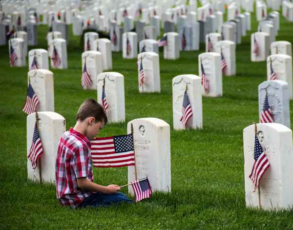 boy in red and white plaid shirt sitting on green grass field near a tombstone