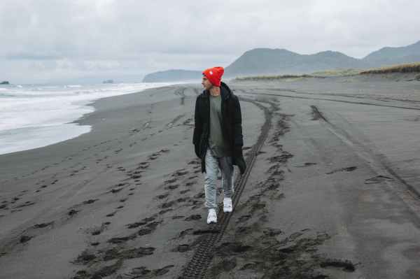 male tourist walking along empty beach and admiring view on ocean